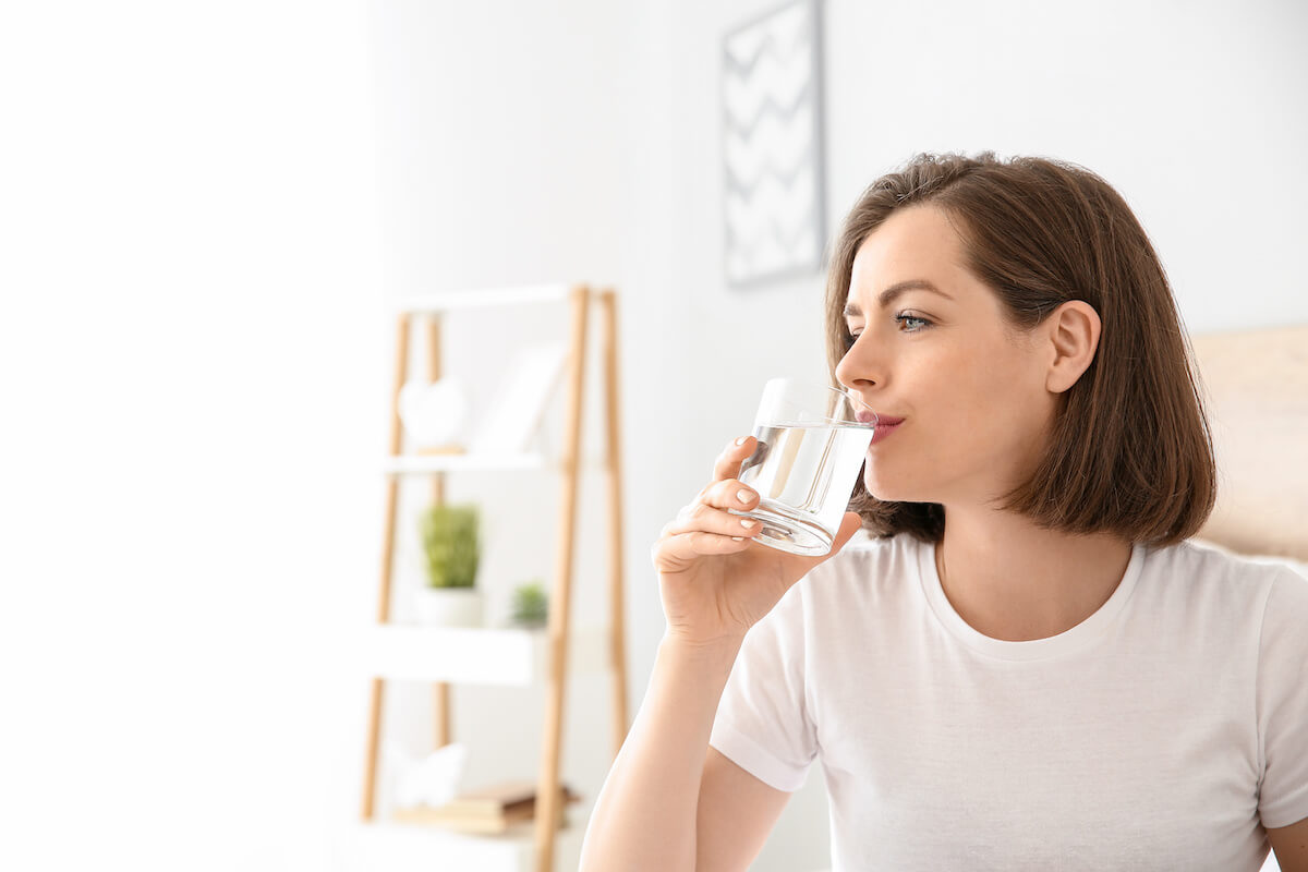 Morning of beautiful young woman drinking water in bedroom