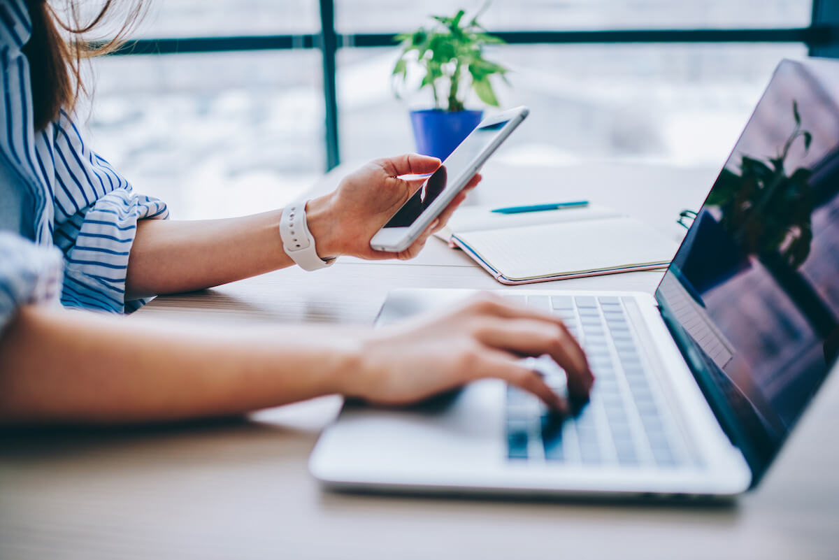 Cropped image of female holding smartphone getting message with confirmation making transaction on laptop computer,woman using mobile phone app for synchronizing data with netbook via bluetooth