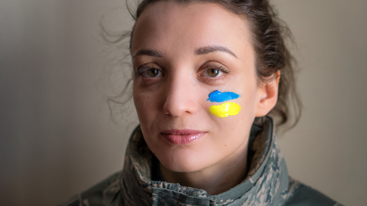 Indoor portrait of young girl with blue and yellow ukrainian flag on her cheek wearing military uniform, mandatory conscription in Ukraine, equality concepts.