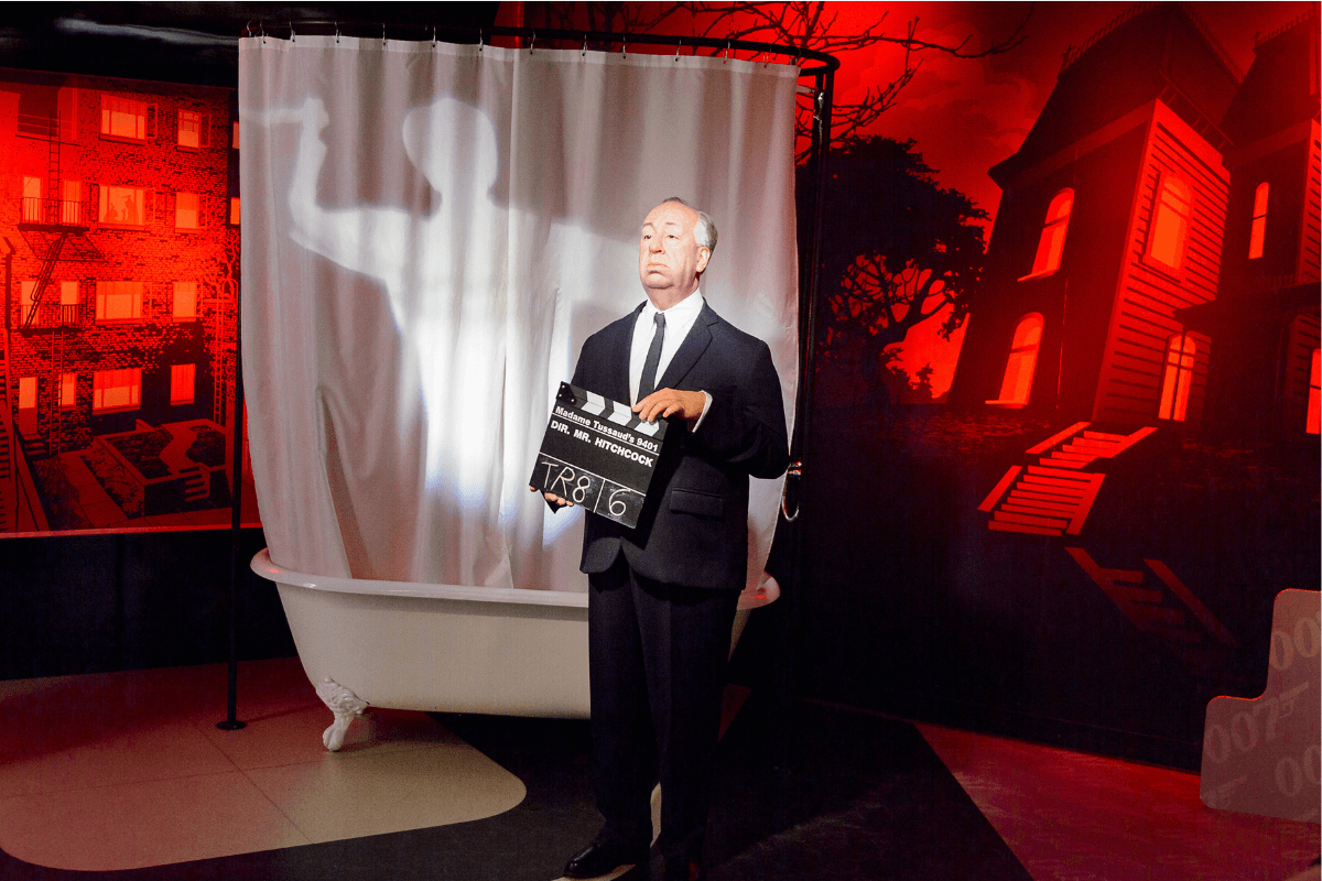 A suited man holding a movie slate board representing Mr Hitchcock movie