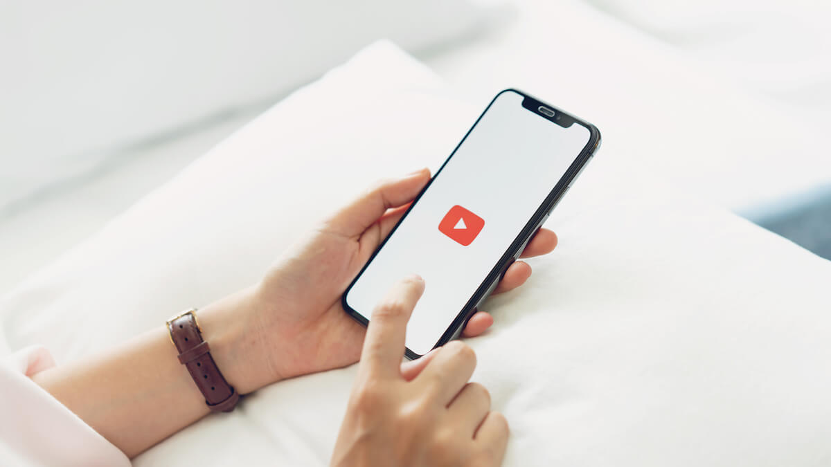 hand is pressing the screen displays the Youtube app icons on Apple iPhone. YouTube is the popular online video-sharing website.