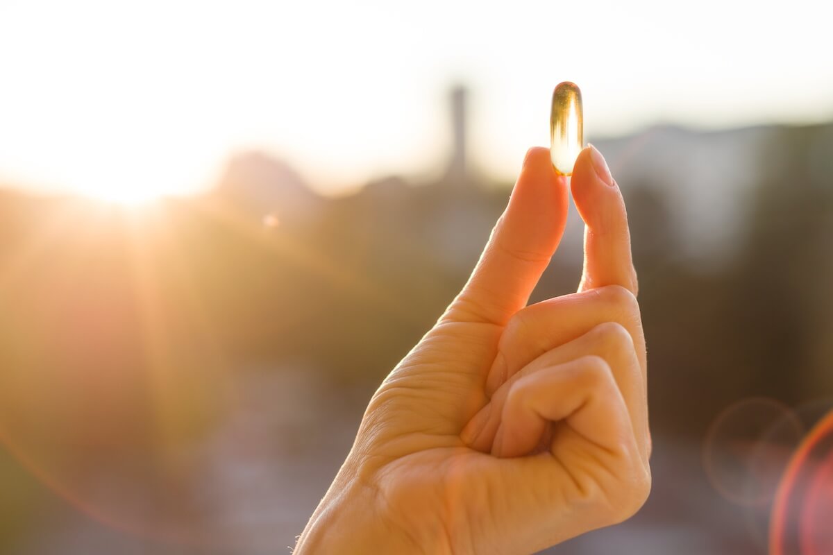 Hand of a woman holding vit D capsule, urban sunset background. Healthy eating, medicine, health care, food supplements and people concept