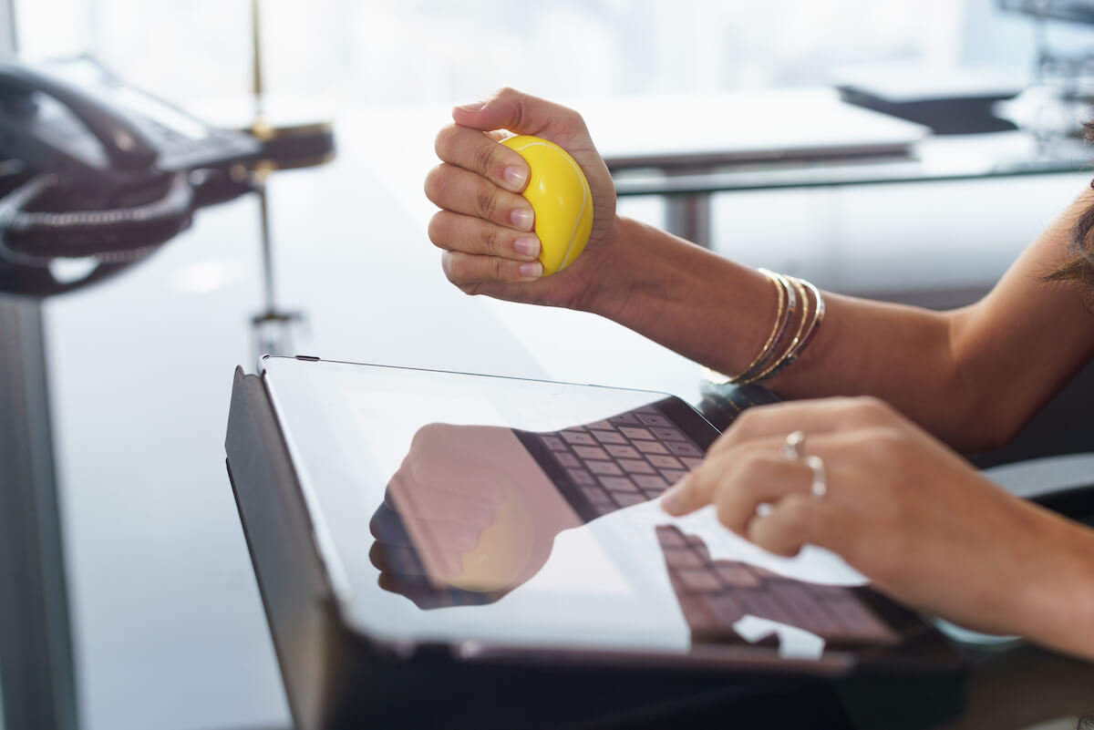 Office worker typing email on tablet computer. The woman feels stressed and nervous, holds an antistress yellow ball in her hand