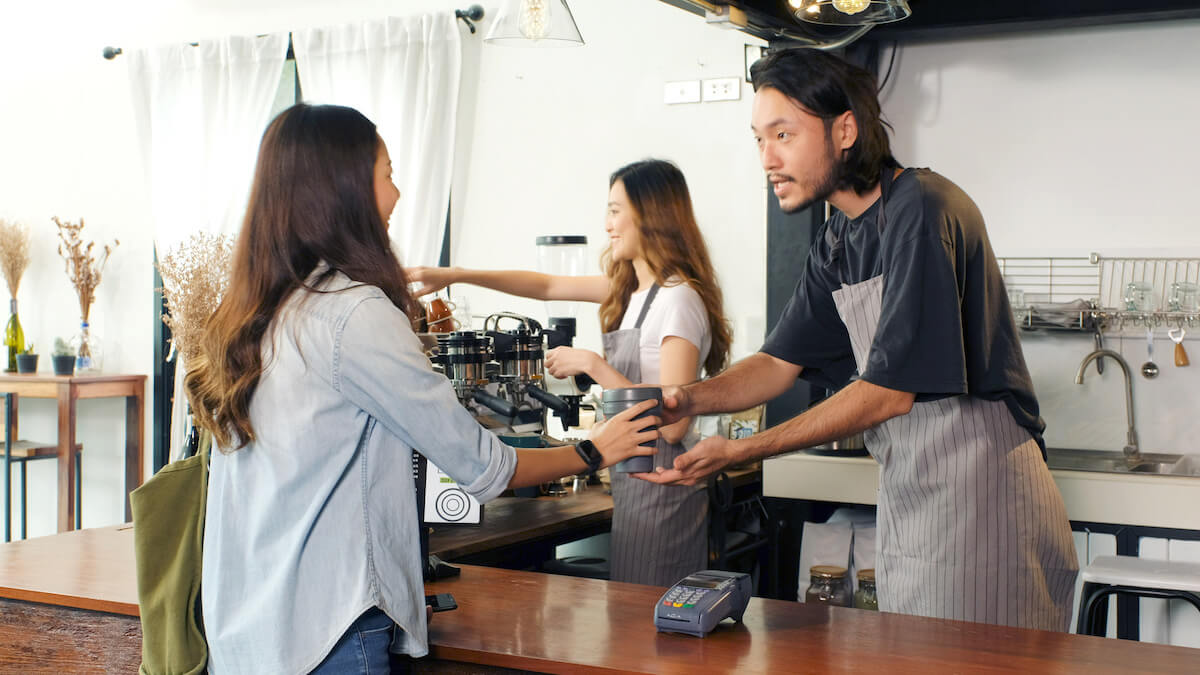 Asian woman customer giving her own coffee cup to barista, waiter, for buying takeout coffee at cafe counter. 