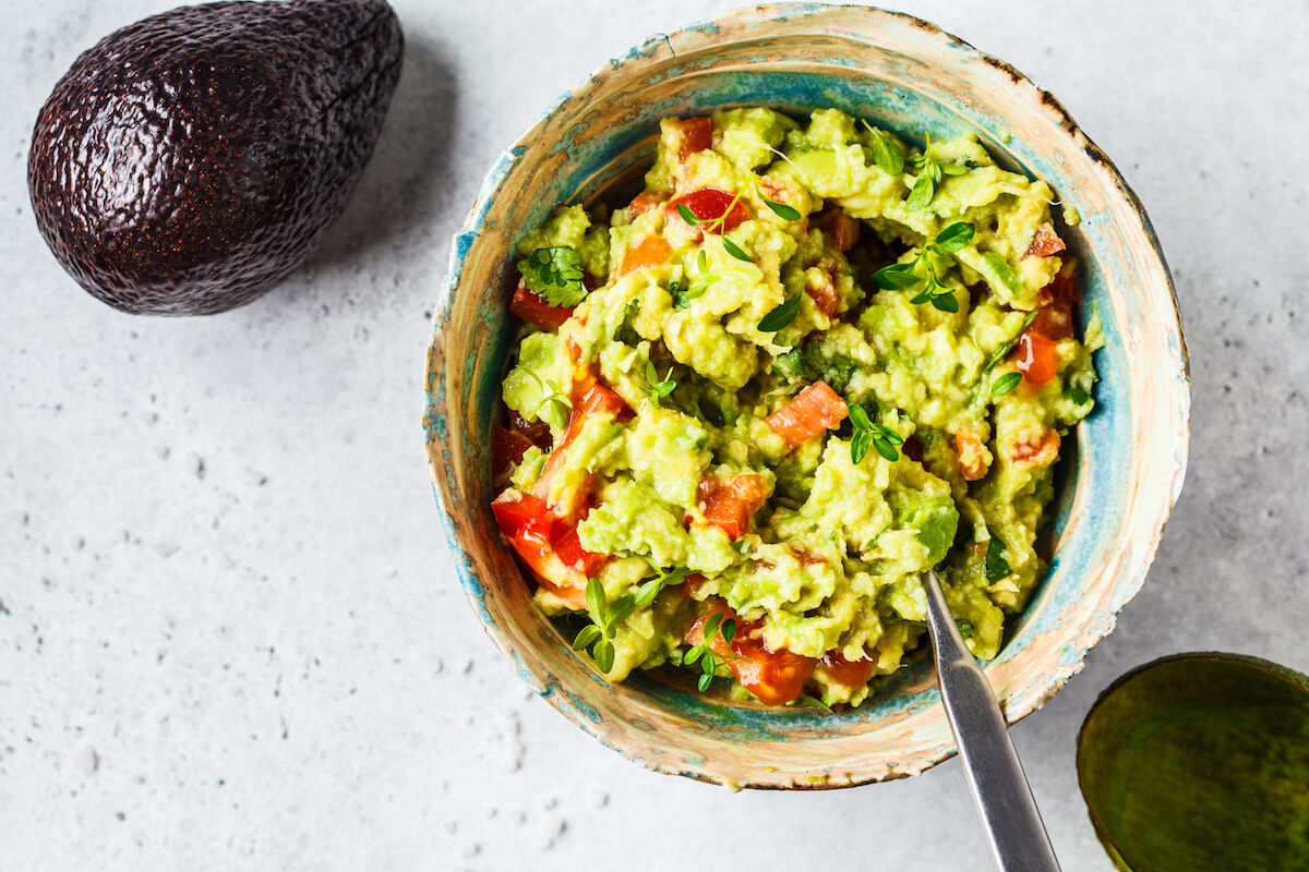 Fresh avocado tomato guacamole in a bowl, top view. 