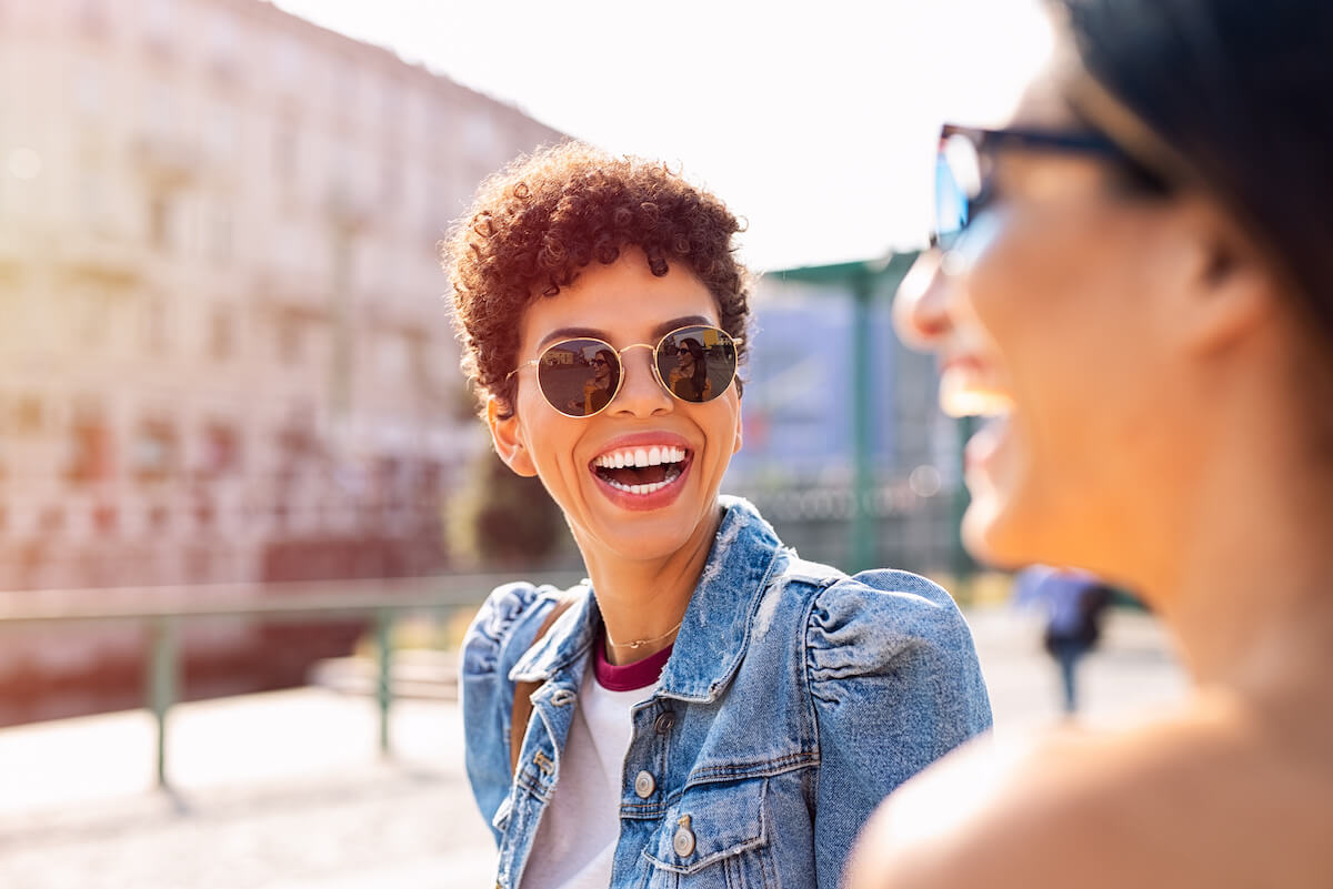 Two beautiful girls having fun on the street. Portrait of young brazilian woman wearing sunglasses smiling at friend on the street.