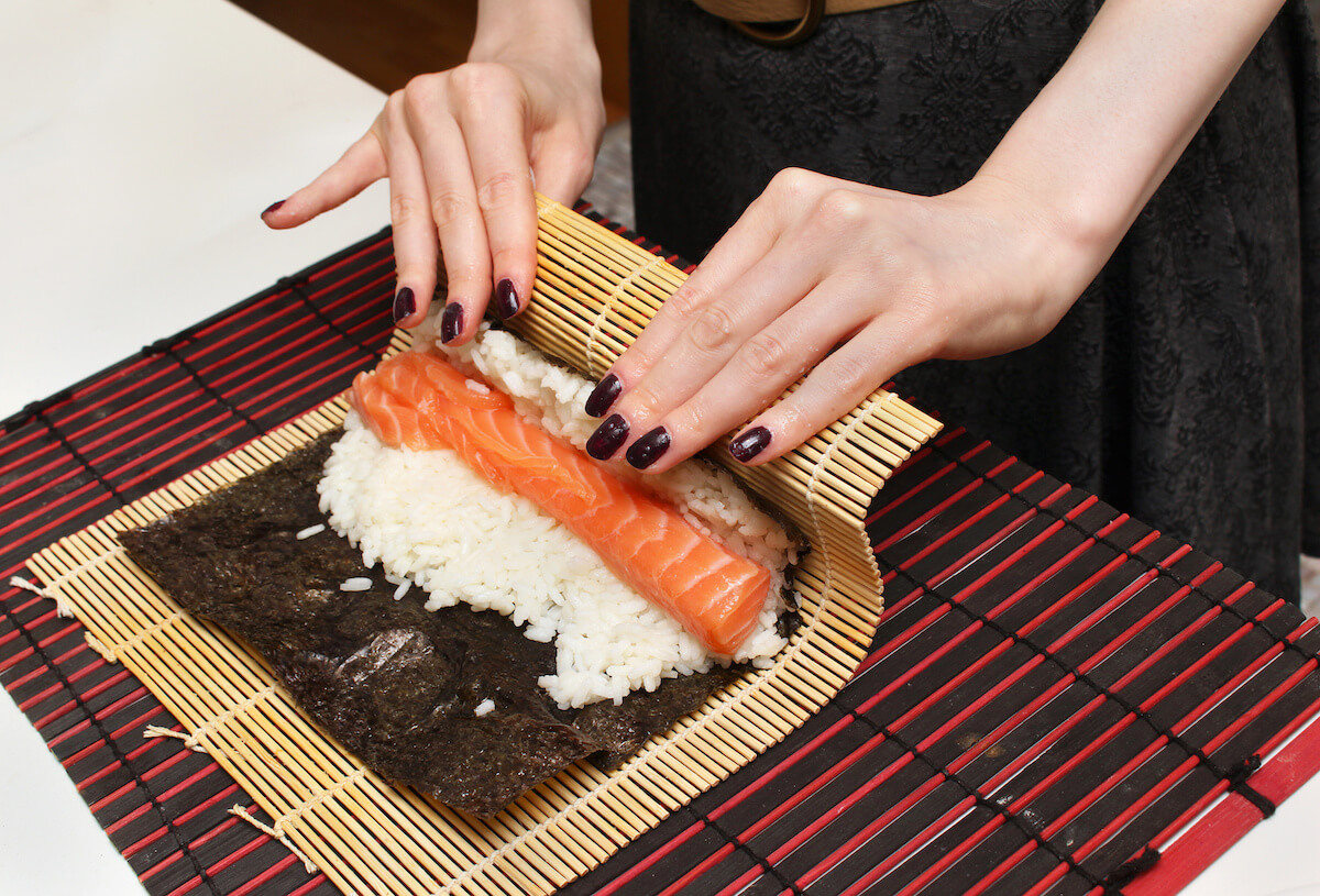 Woman using bamboo rolling mat for home made sushi.