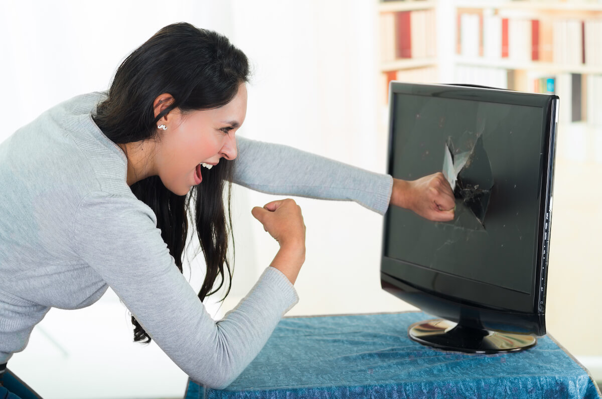 Angry female brunette punching computer screen with large hole on it