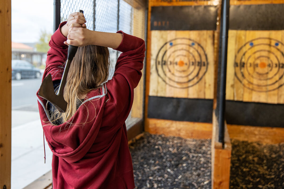 Young girl throws an axe at a target in an axe throwing range.