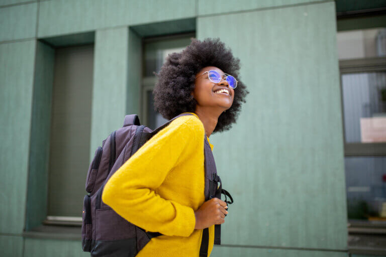 happy african female college student with glasses and bag