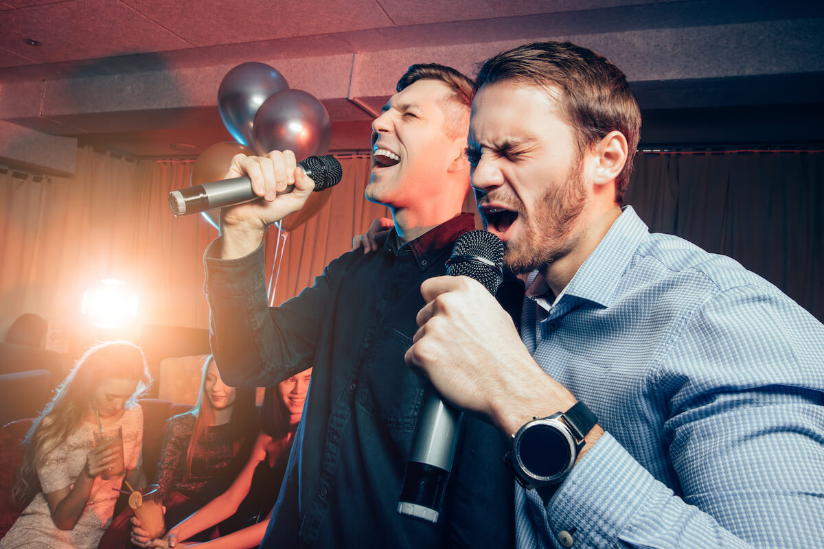 Two young caucasian men singing in microphone in karaoke bar.