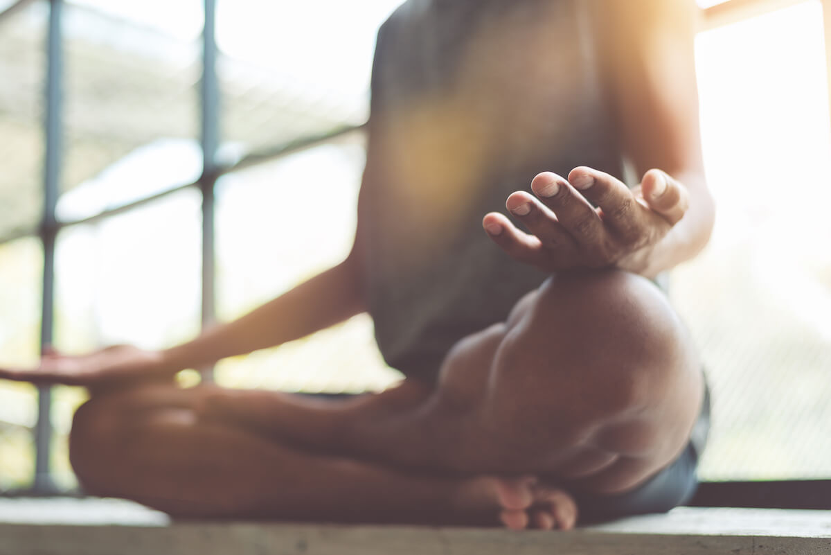 Male practicing meditation indoors cross-legged.