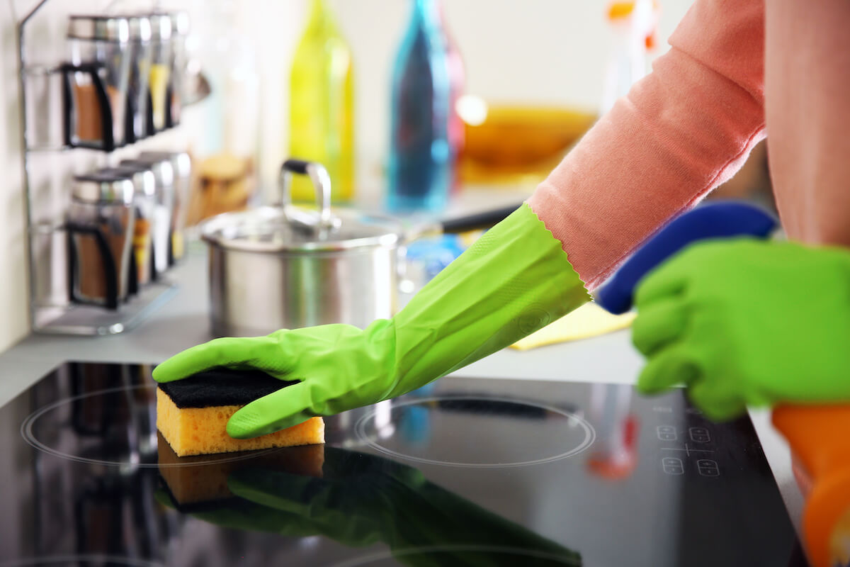 Human hand in protective gloves washing electric hob in the kitchen.