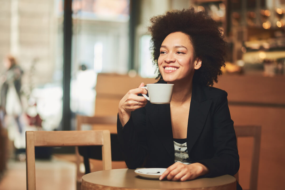 Mixed race woman drinking coffee and smiling. 