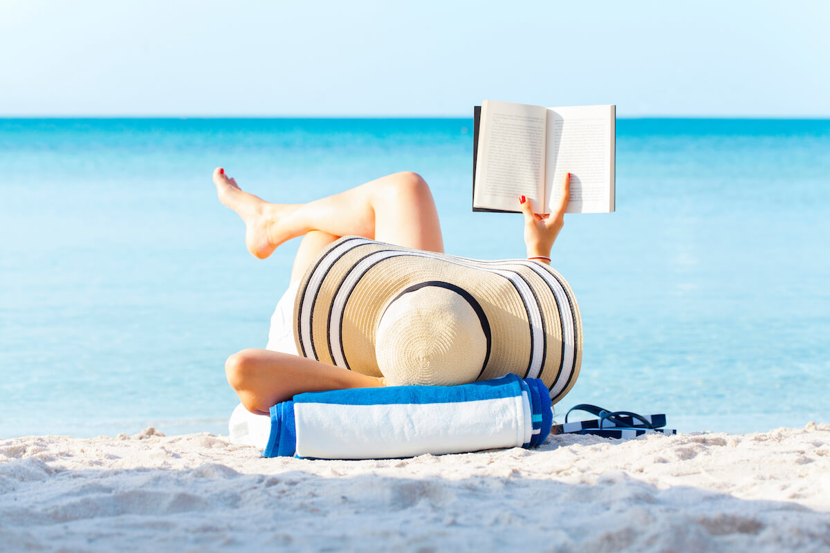 Portrait of a young brunette relaxing on the beach, reading a book.