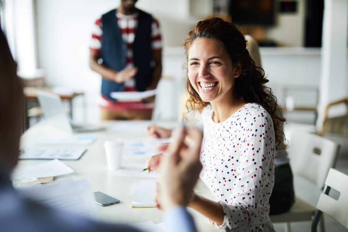 Happy young businesswoman sitting at desk and communicating with her colleagues during a meeting.