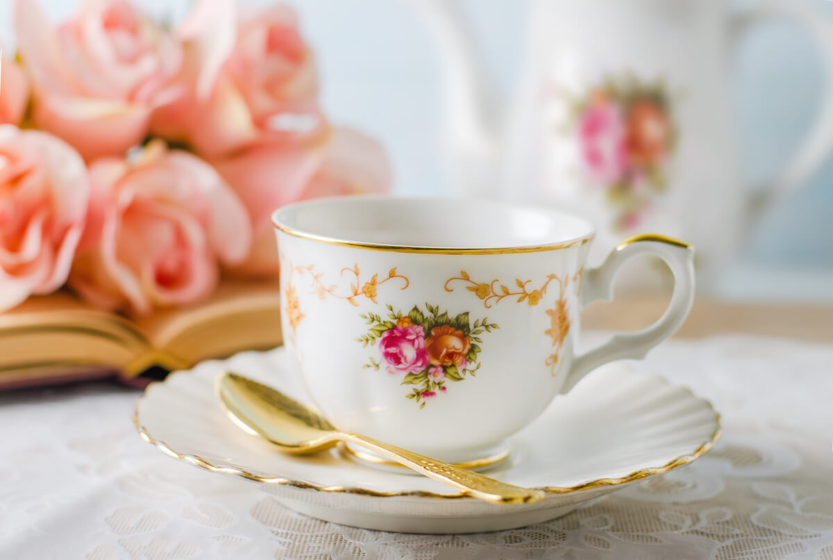 Close up of cup of tea with book, teapot and rose flowers on blue background with vintage tone