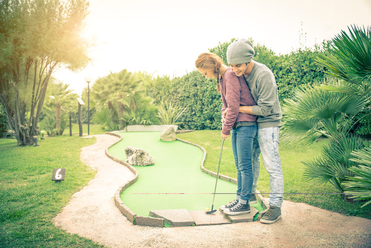 Boyfriend teaching to his girlfriend how to putt at a mini golf club.