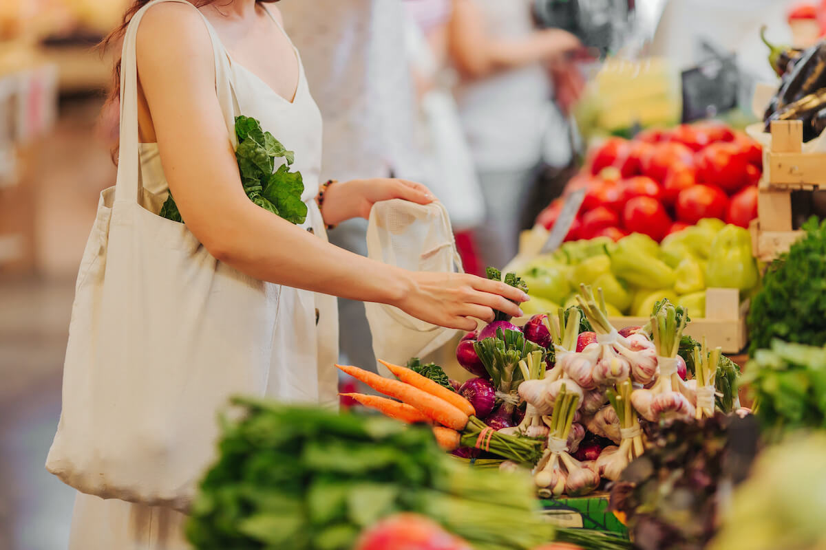 Female hands puts fruits and vegetables in cotton produce bag at food market. Reusable eco bag for shopping. Zero waste concept.