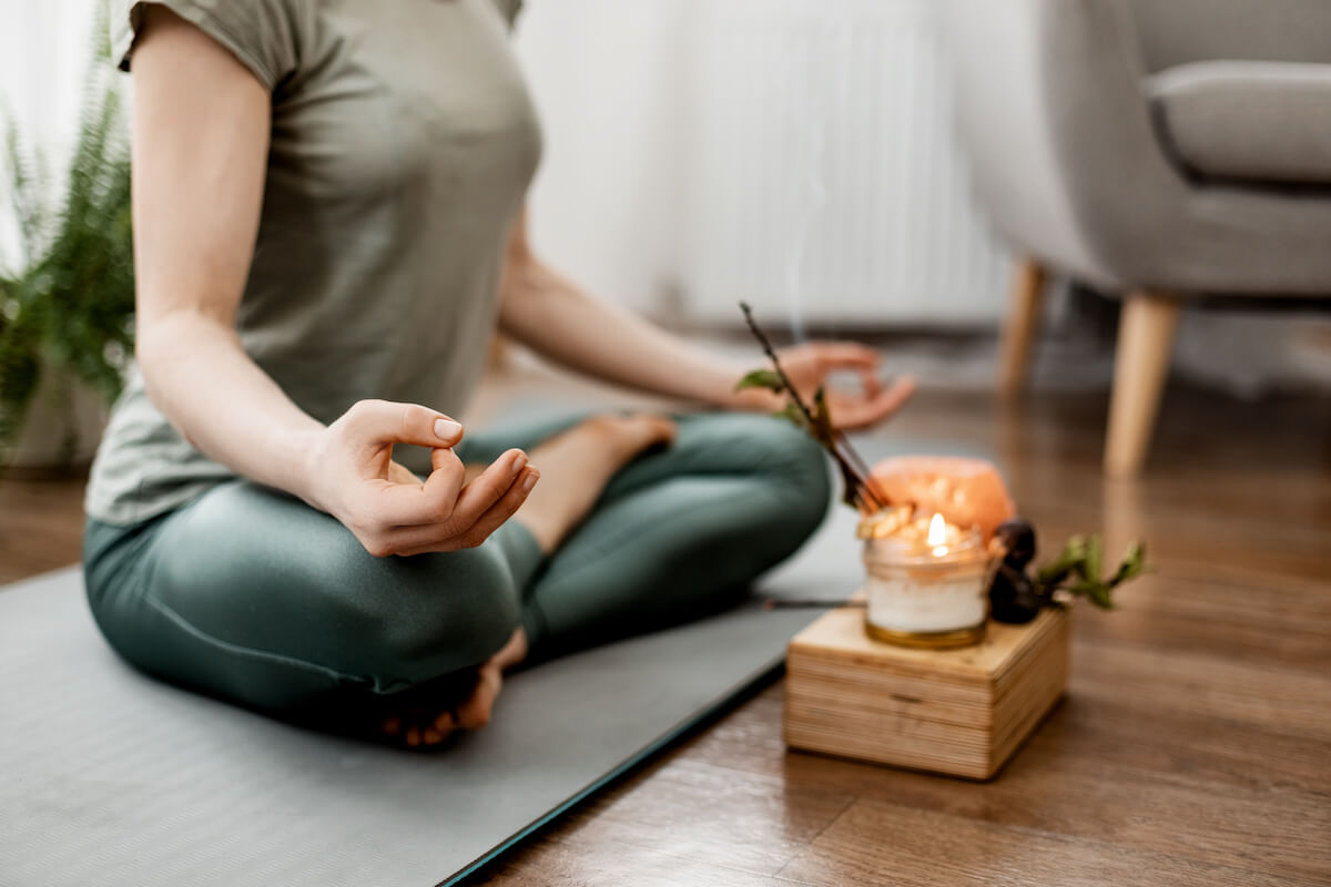 Young relaxed woman doing yoga at home with candles and incense, close-up of hands.