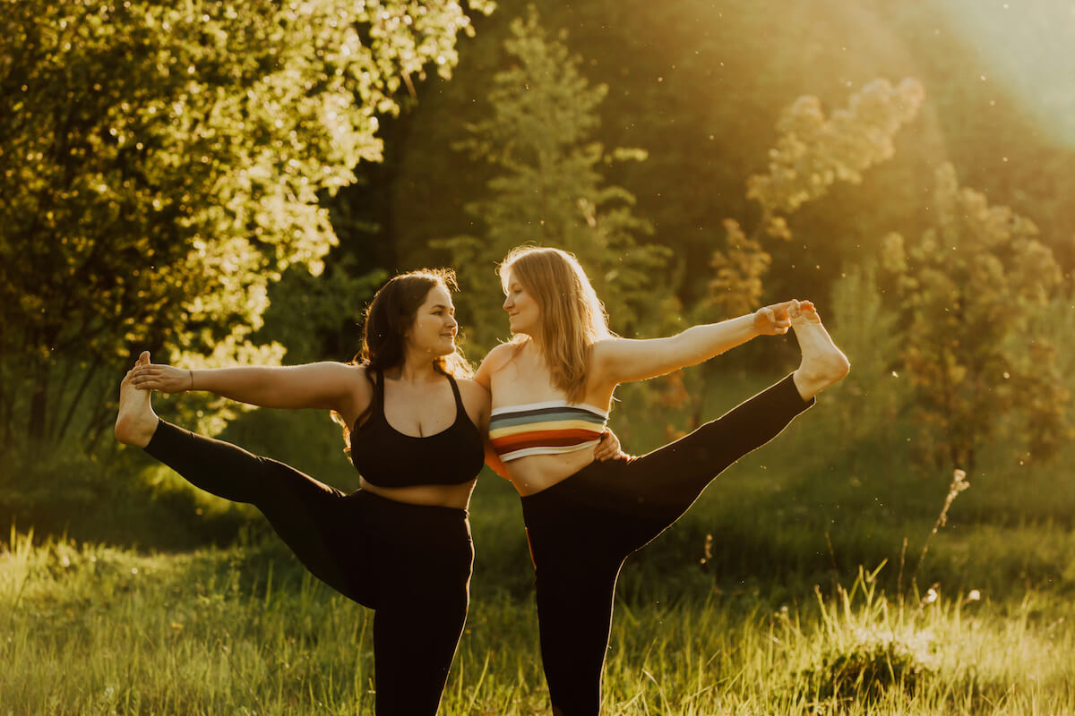 Two beautiful women with long hair doing yoga in nature on a sunny summer day.