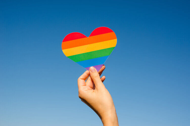 Woman holds in hands a heart in the colors of the rainbow. Young beautiful girl. LGBT history month. Pride Month. Lesbian Gay Bisexual Transgender. LGBT flag. Love, human rights, tolerance.