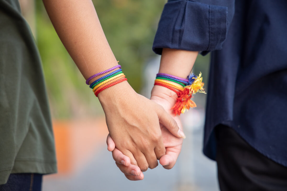 Hand of LGBT women holding together with rainbow ribbon symbol