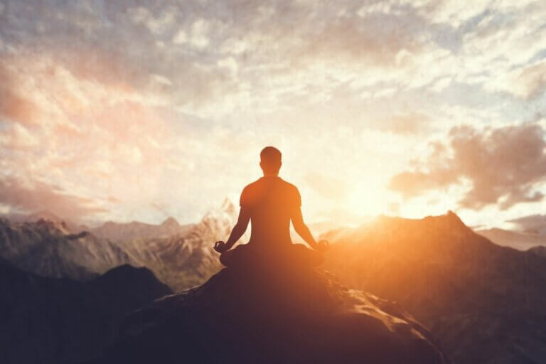 Man meditating on a mountaintop during sunrise