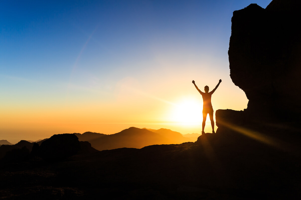 Female hiker with arms up outstretched on mountain top looking at beautiful night sunset inspirational landscape.