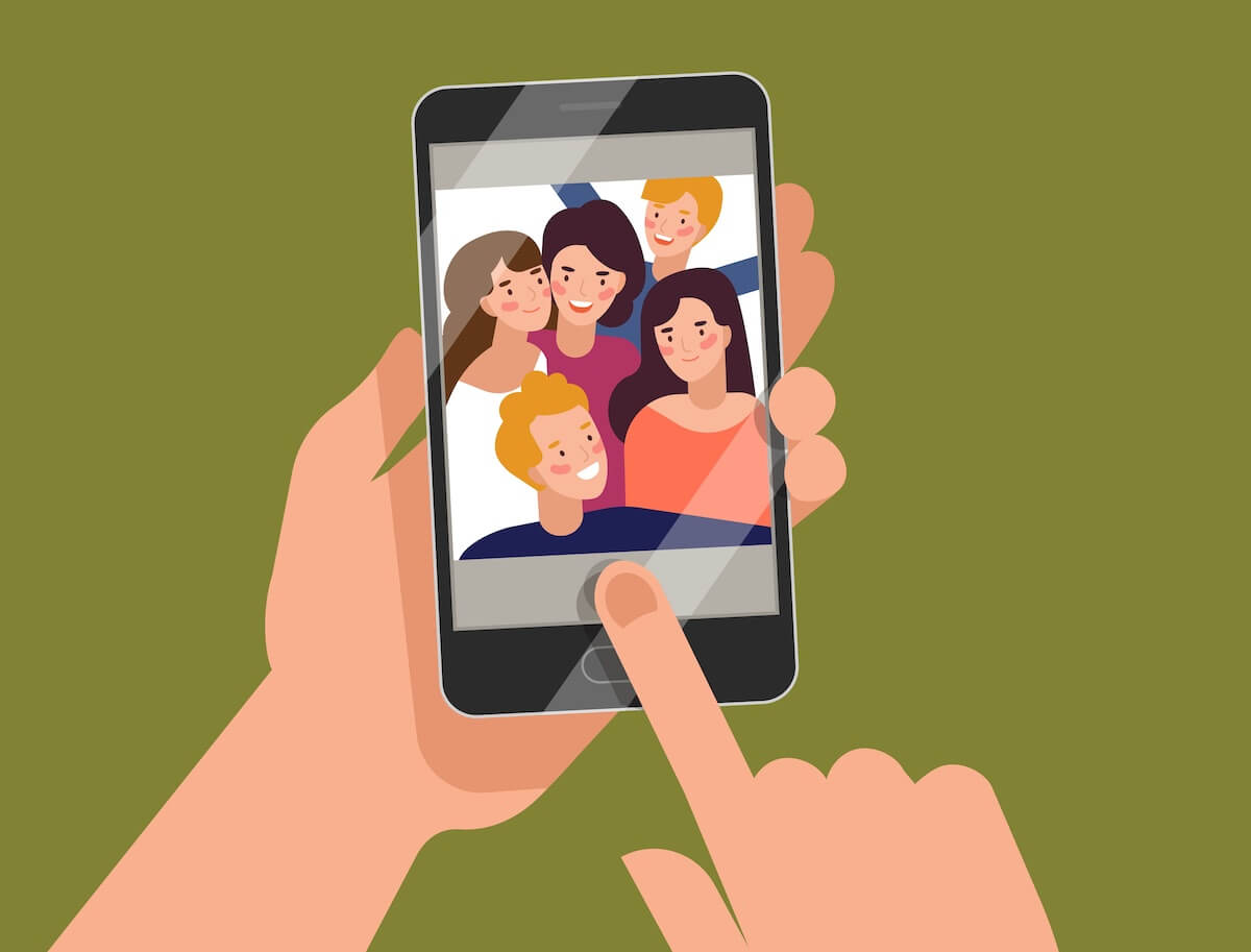 Hands holding smartphone with young smiling men and women displaying on screen. Friends taking selfie, group of happy people photographing themselves.