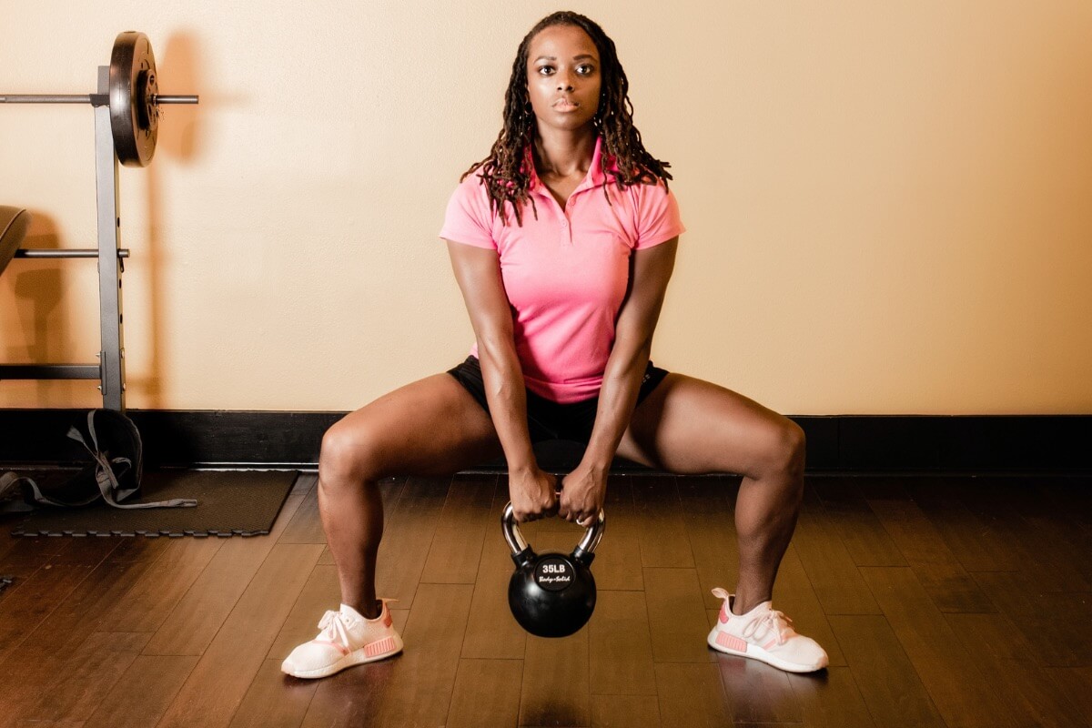 Black female doing squats with kettlebell. 