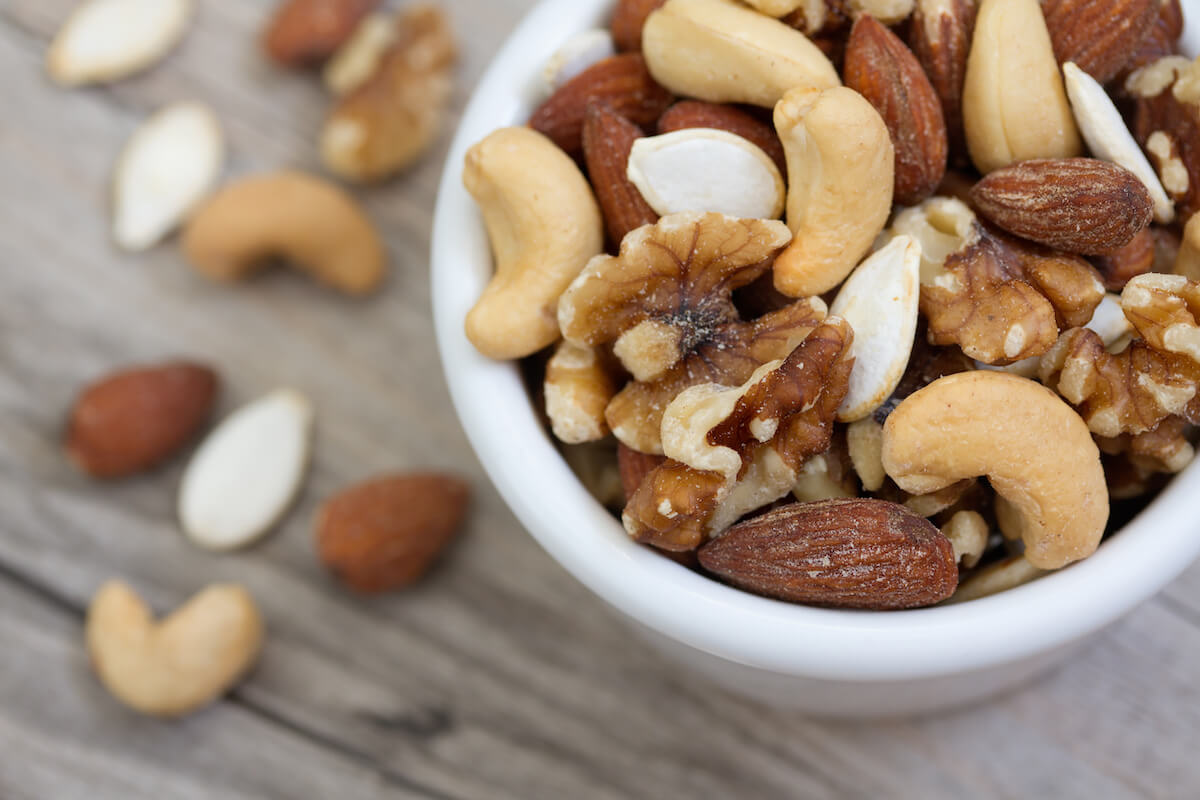 Bowl of mixed nuts on rustic wooden table in natural light.