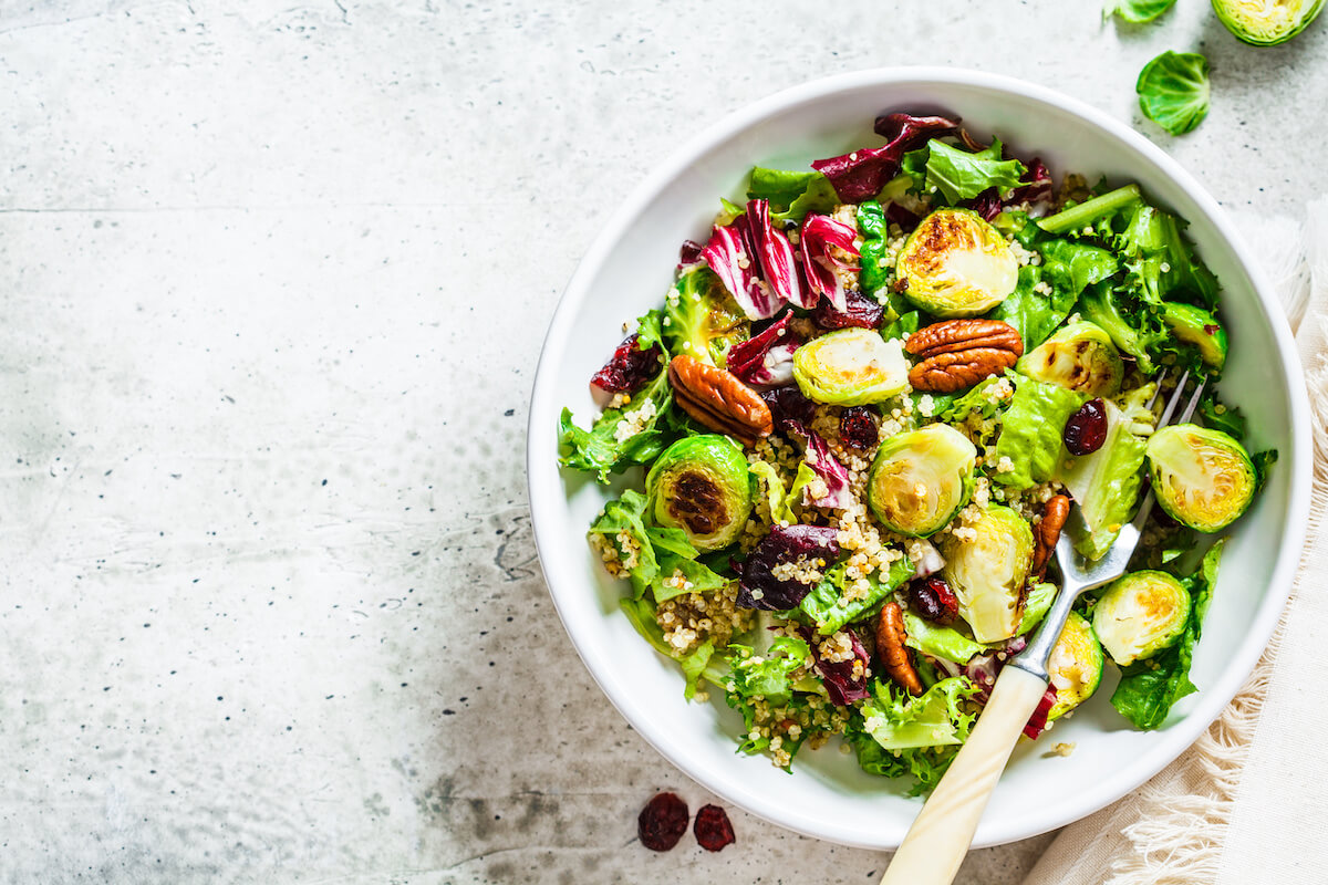 Fried brussels sprouts salad with quinoa, cranberries and nuts in a white bowl