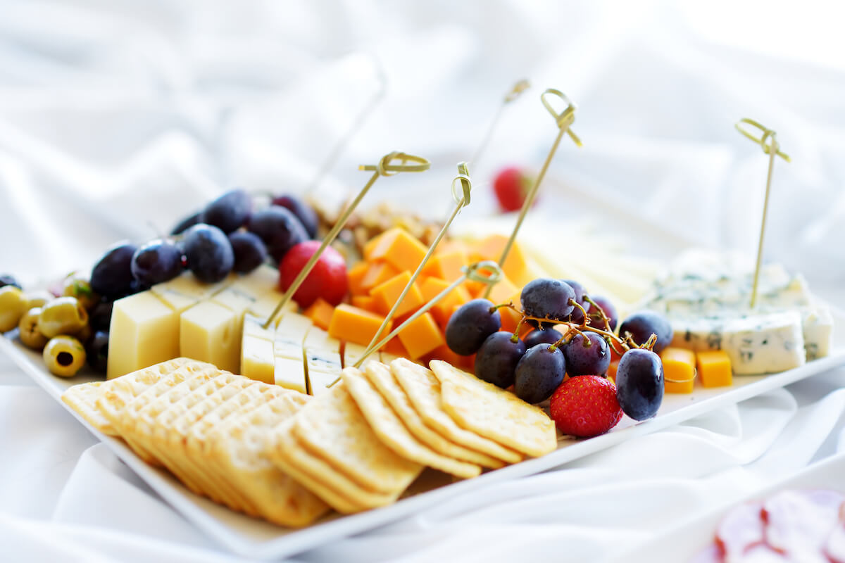 Different kinds of wine snacks: cheeses, baguettes, crackers, fruits and olives on white table