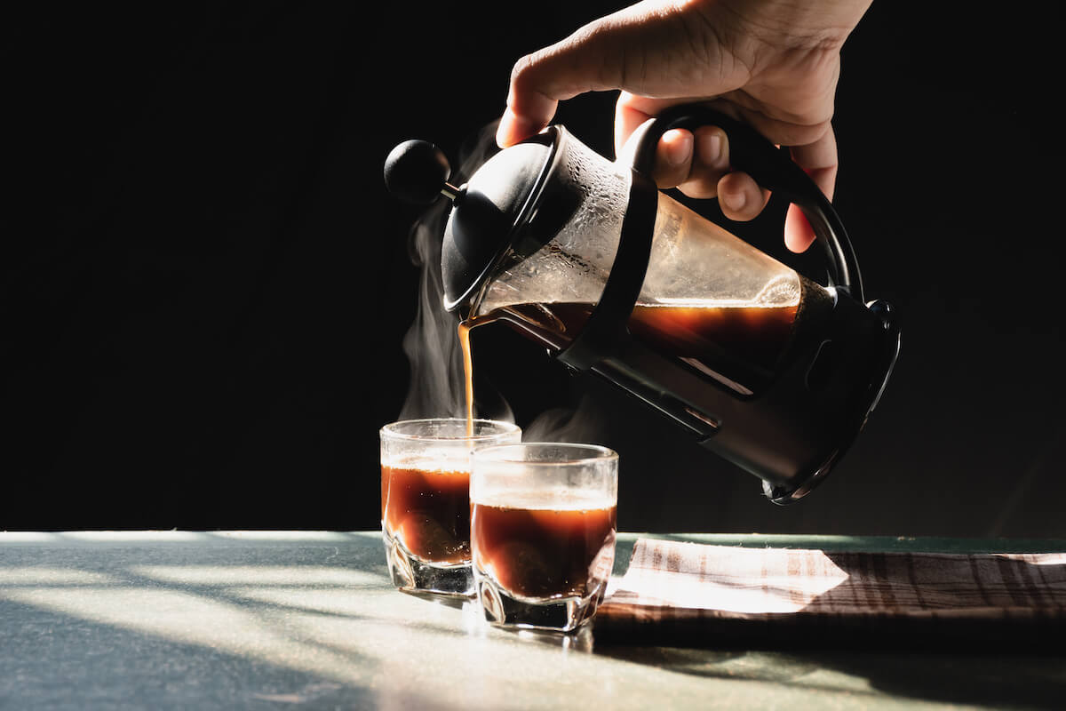 Aromatic coffee with hot smoke are poured into couple cup from French press coffee maker