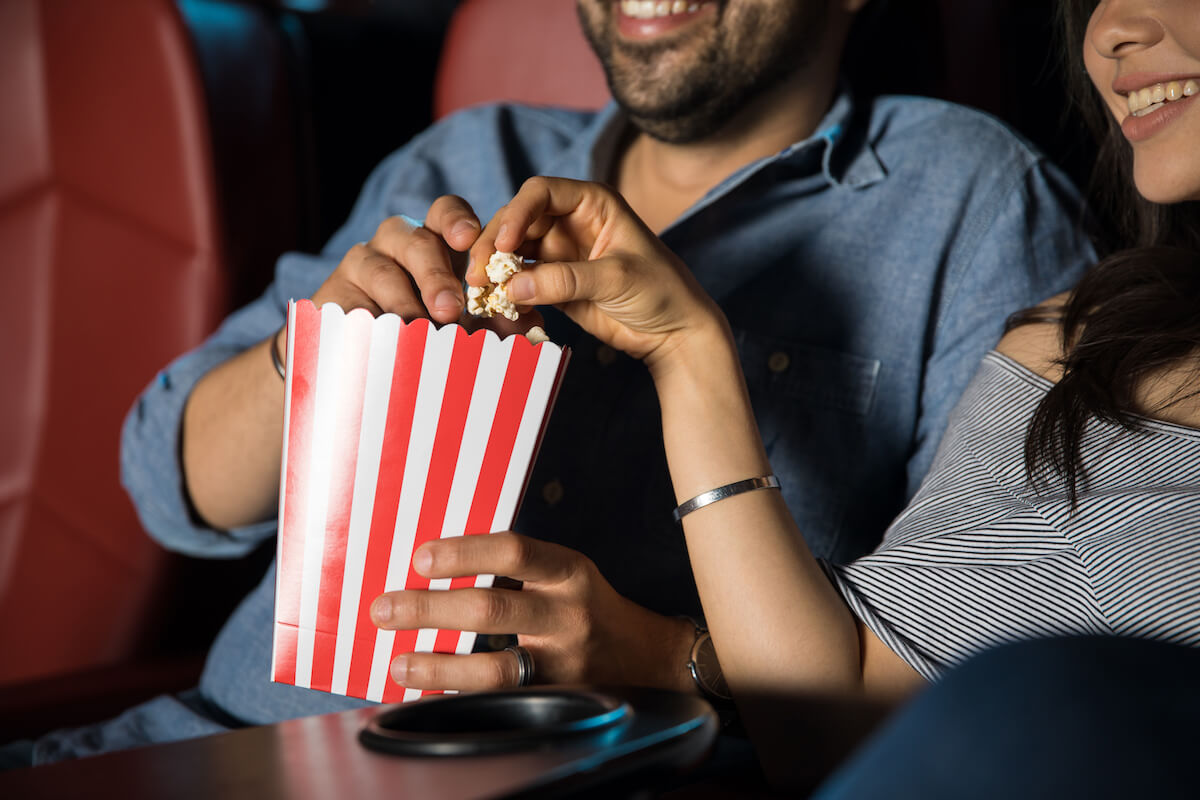 Man touching the hand of his date while grabbing some popcorn at the movie theater