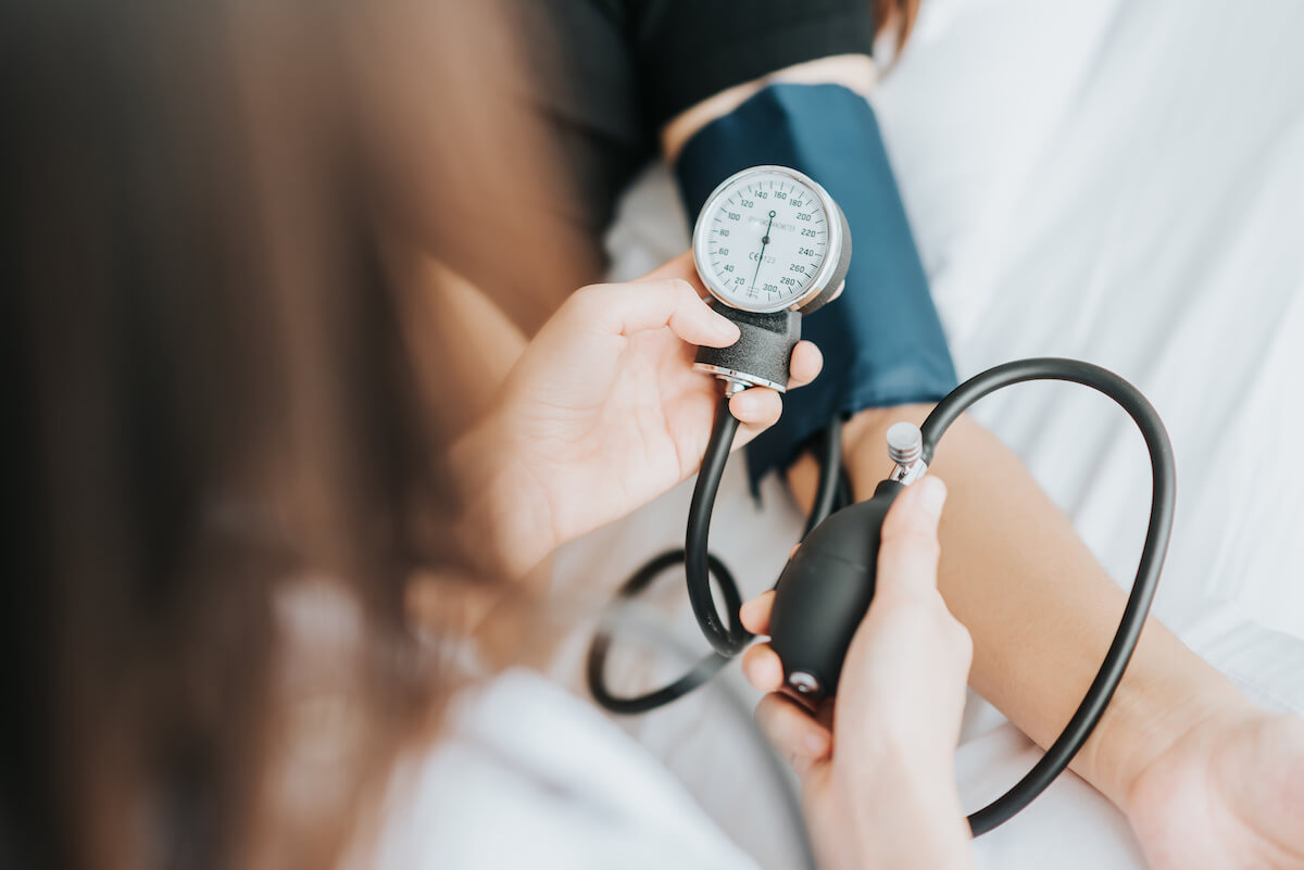 Back view of doctor checking blood pressure of a patient with sphygmomanometer in bed