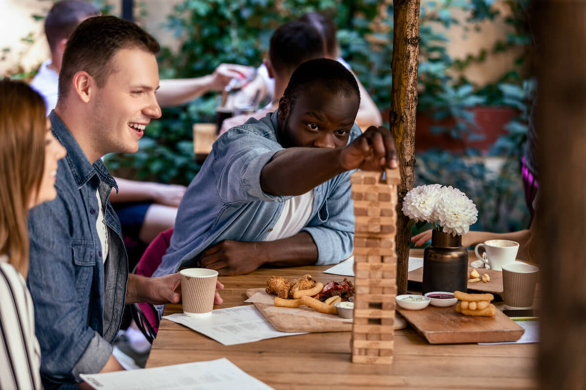 African male is playing table game jenga with caucasian best friends at the local cozy restaurant
