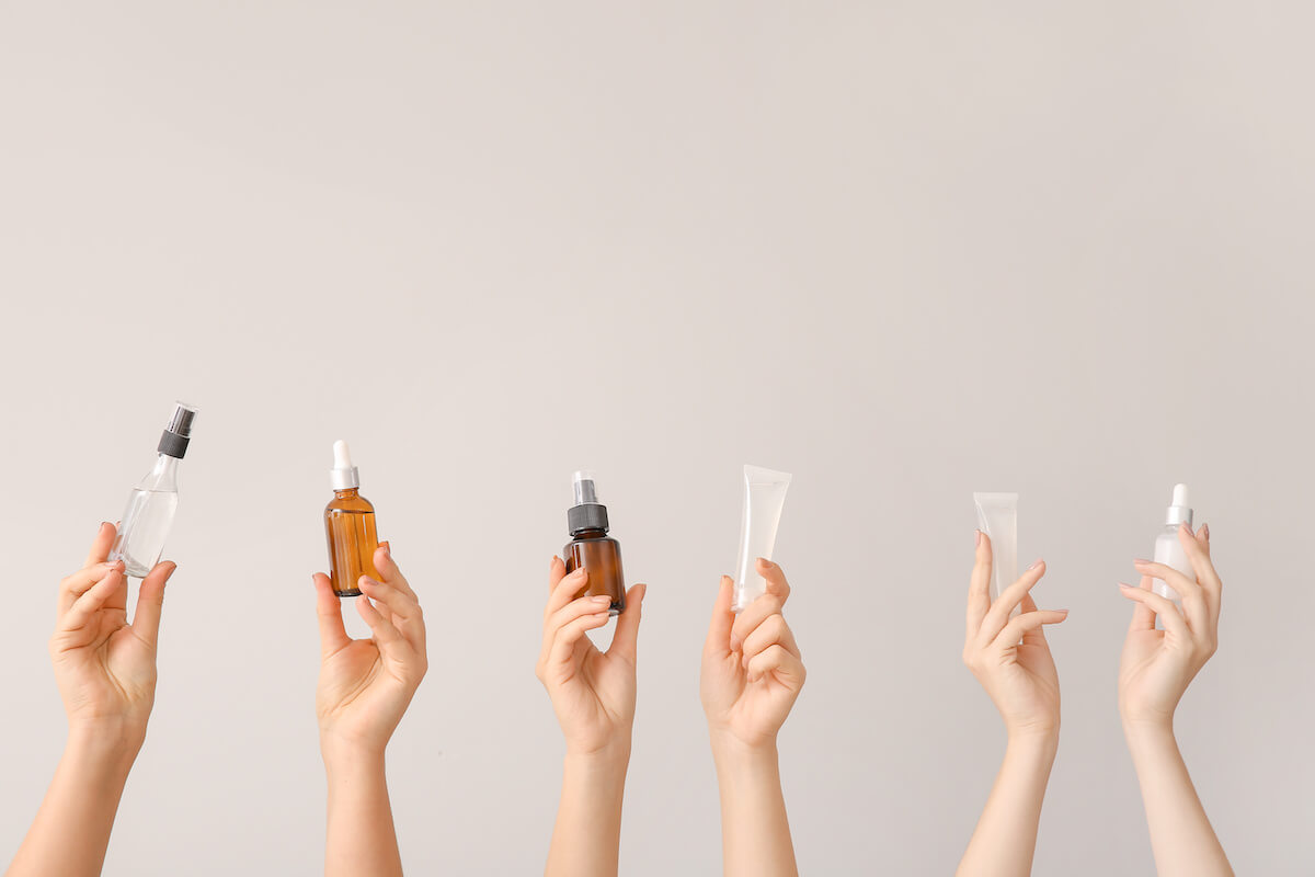 Female hands with different cosmetic products in bottles on grey background