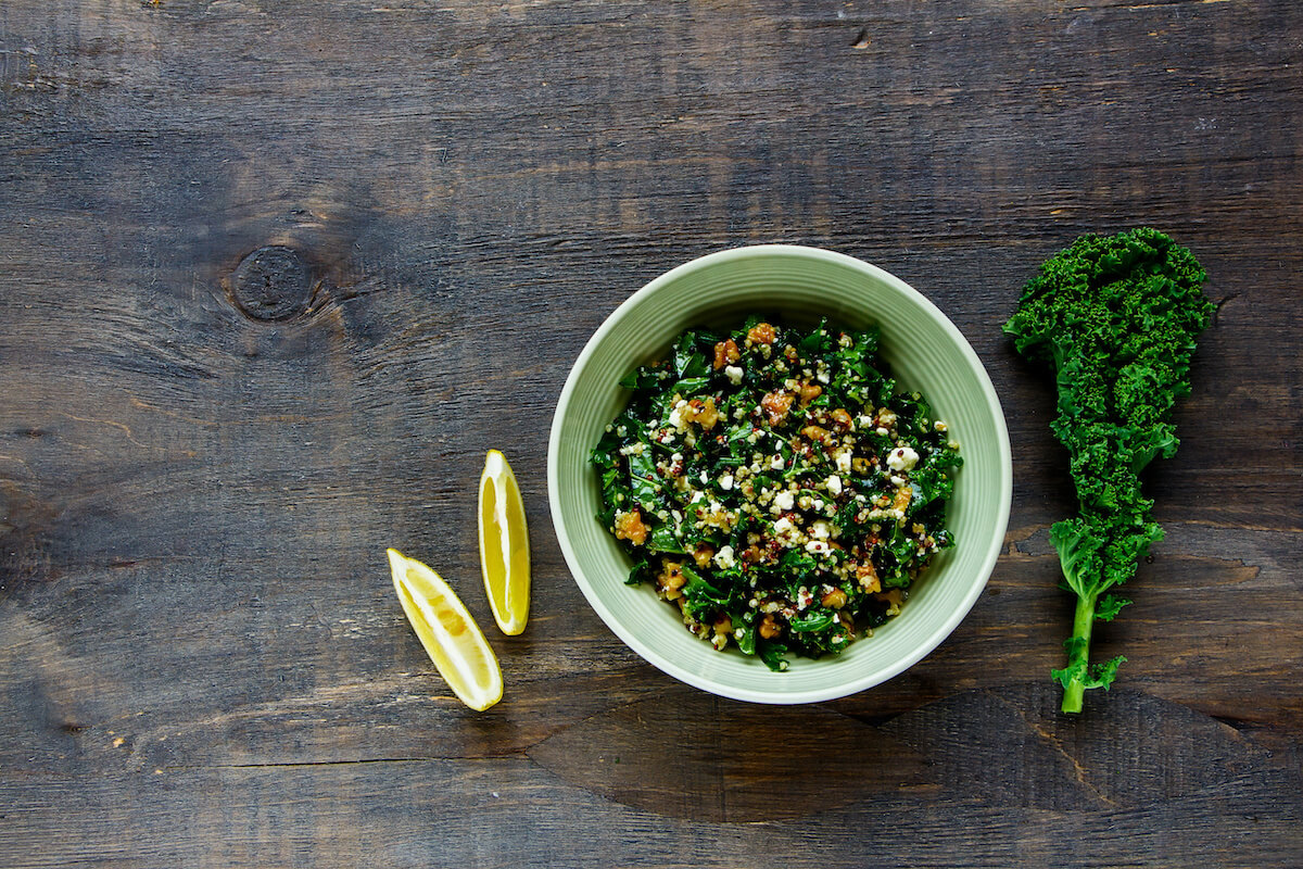 Detox salad bowl flat lay. Healthy raw kale and quinoa salad with feta cheese and walnut on wooden background.