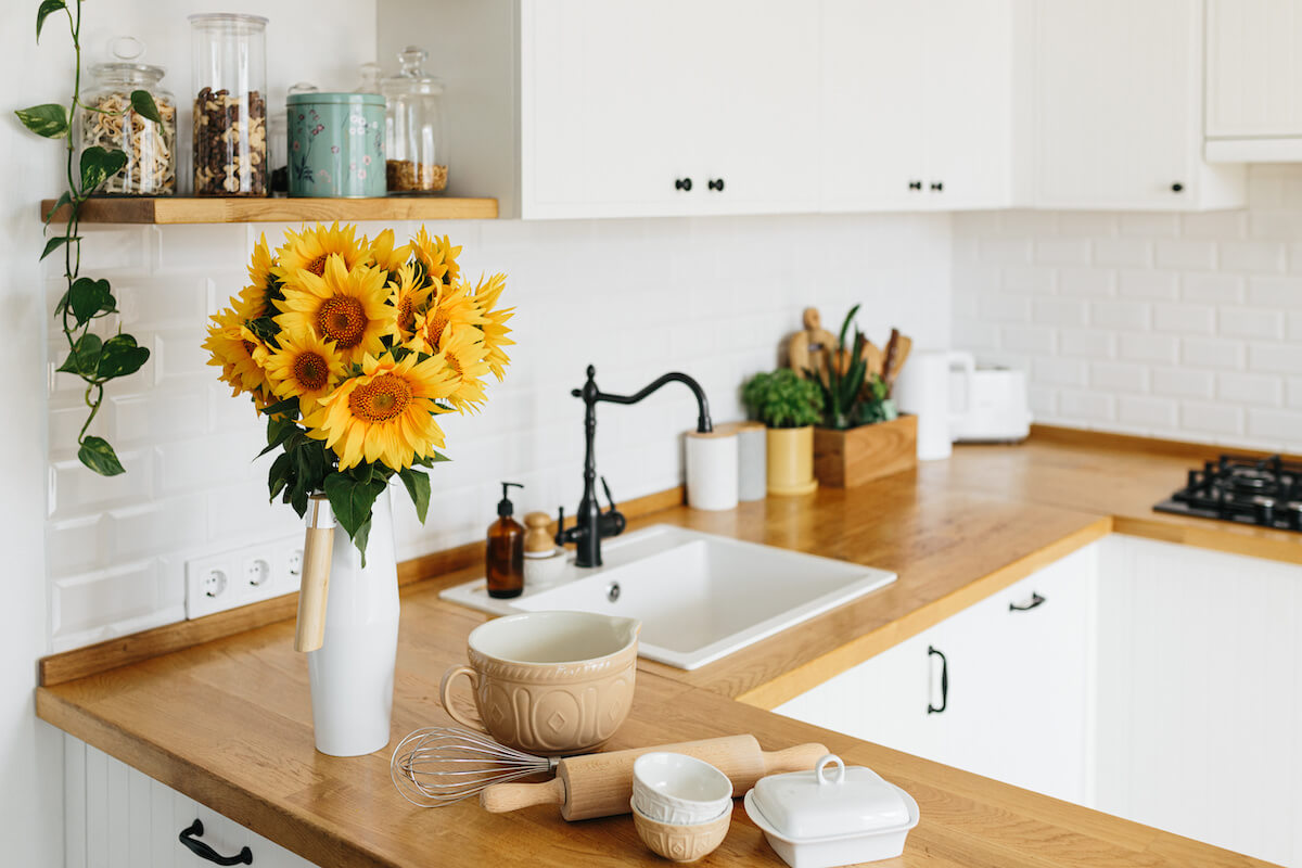 White simple modern kitchen in scandinavian style, kitchen details, wooden table, sunflowers bouquet in vase on the table