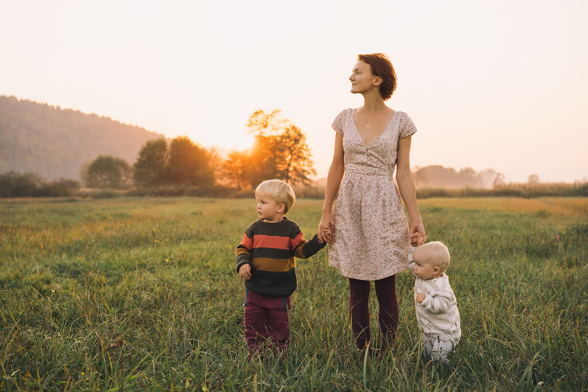 Young mother with children in sunlight at sunset on nature outdoors.