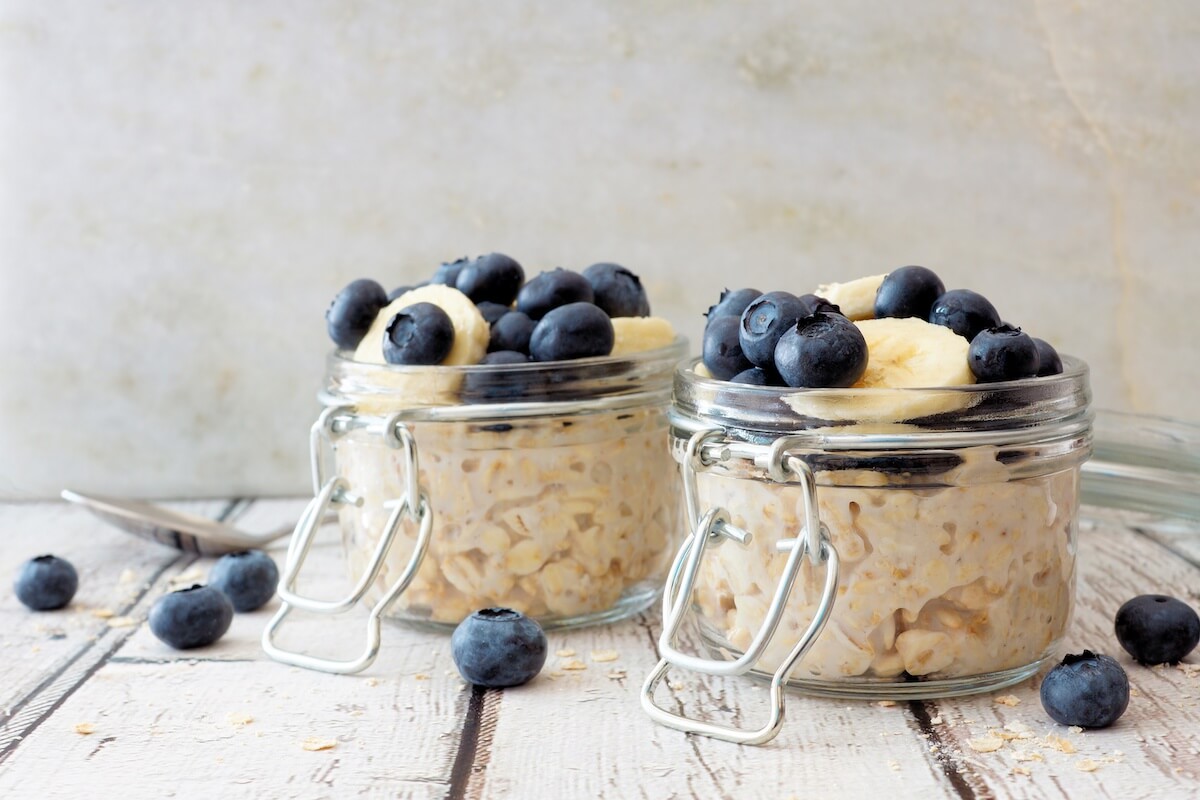 Overnight oats with fresh blueberries and bananas in jars on a rustic white wood background