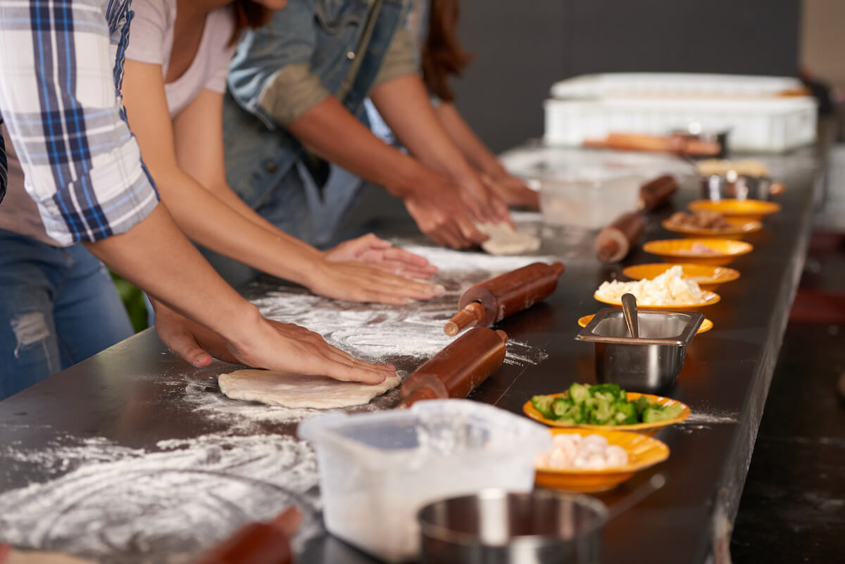 Hands of people making pizzas together in cafe kitchen