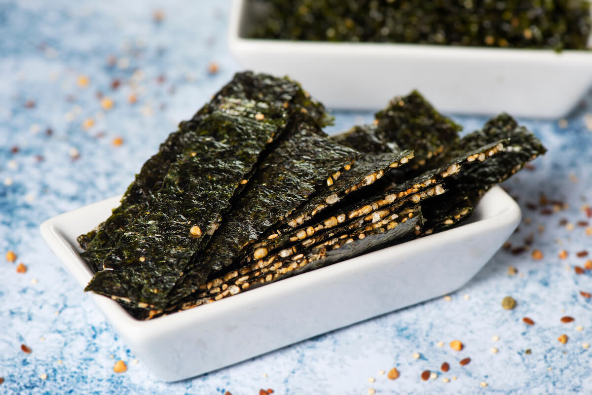 snacks made with seaweed and crispy rice on a rectangular white ceramic bowl, placed on a stone table or countertop