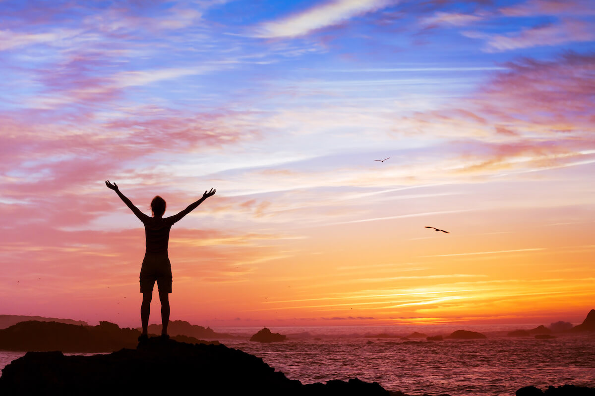 Silhouette of woman with raised hands on beautiful sunset background.