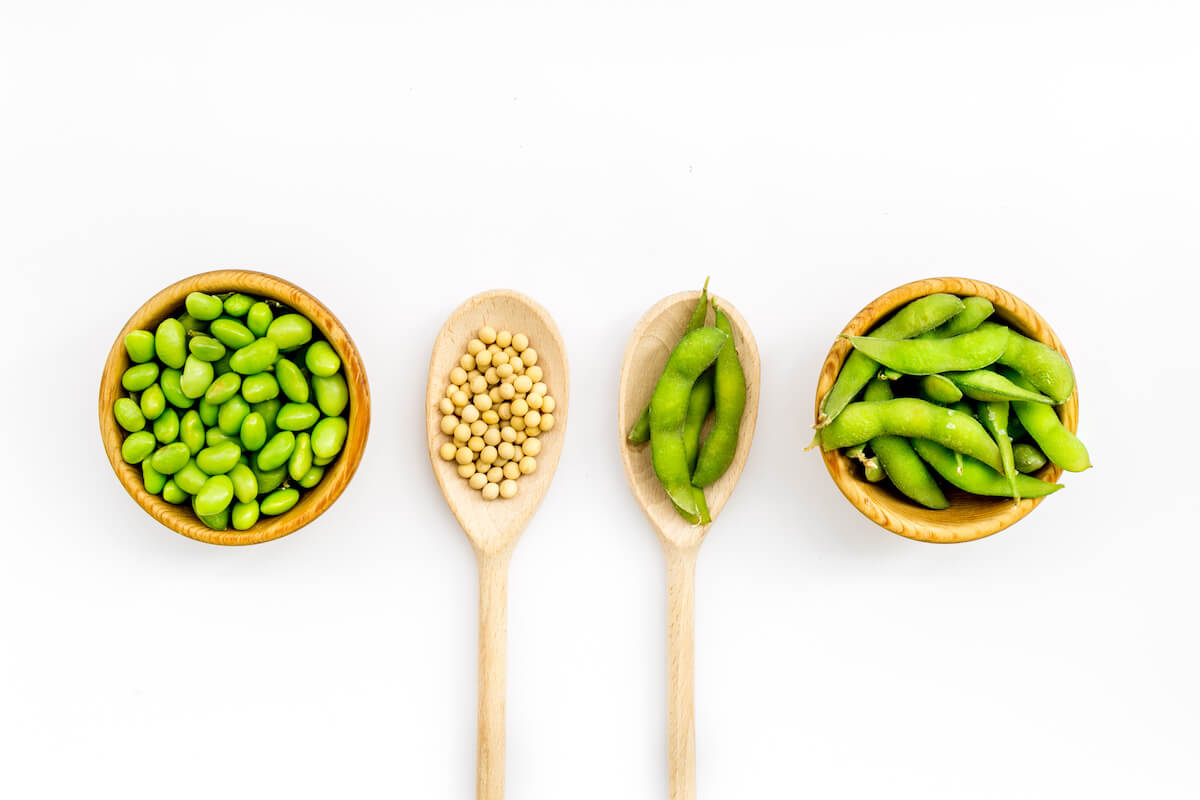 vegan food concept with green soybeans or edamame in spoon and bowl on white desk background top view