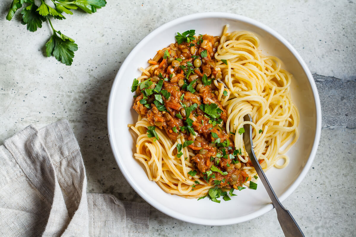 Vegetarian lentils bolognese pasta with parsley in a white dish. 