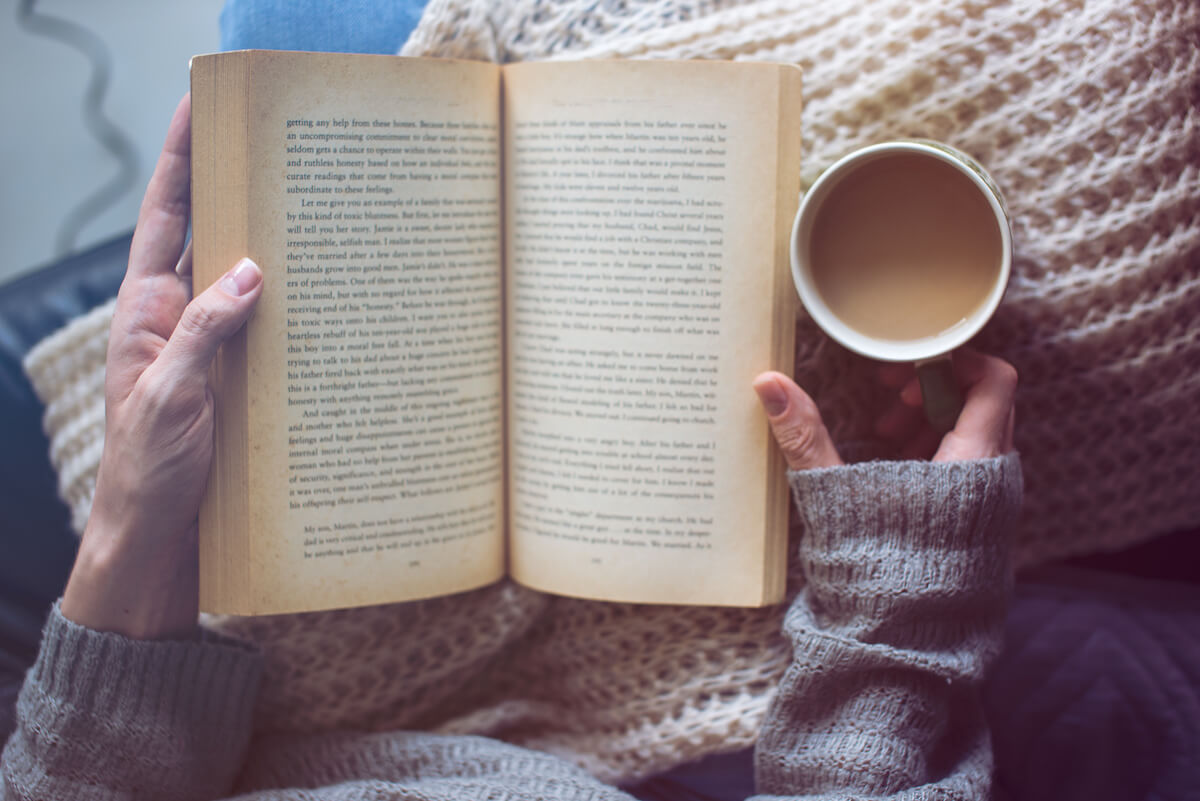 Woman is reading a book and holding coffee