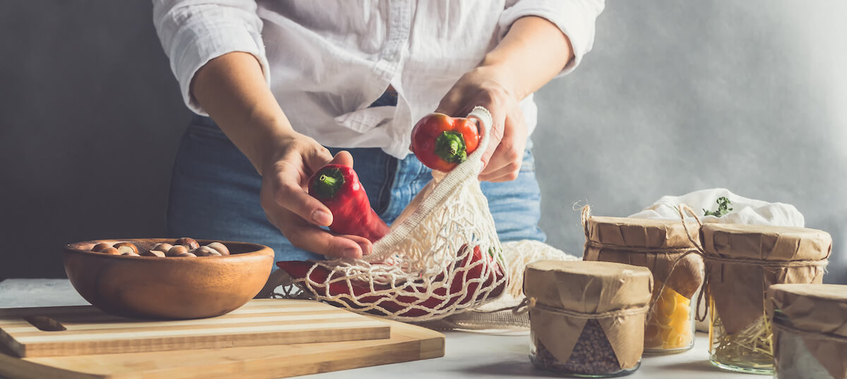 Woman in a white shirt pulls peppers from a knitted rag bag for shopping in the Scandinavian kitchen, zero waste